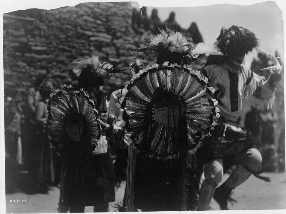 Costumed dancers wearing dance bustles of Tewa sun god made of turkey feathers.