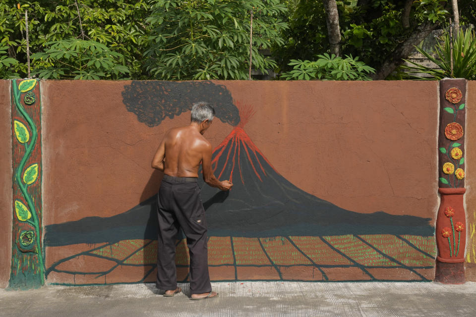 Violeta Peralta paints a picture of an erupting Mayon Volcano outside his home in Legaspi, Albay province, northeastern Philippines, Sunday, June 11, 2023. Thousands of villagers have been forced to leave rural communities within a 6-kilometer radius of Mayon volcano's crater in Albay province which was placed under a state of calamity on Friday to allow more rapid disbursement of emergency funds in case a major eruption unfolds. (AP Photo/Aaron Favila)