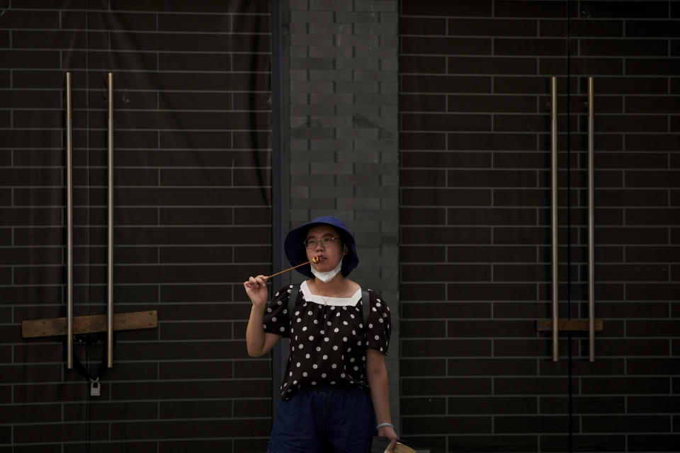 A woman eats a sugar-coated Chinese haw in front of vacant shop lots at Qianmen Street in Beijing, Wednesday, Aug. 17, 2022. Factories in China's southwest have shut down after reservoirs used to generate hydropower ran low in a worsening drought, adding to economic strains at a time when President Xi Jinping is trying to extend his position in power. (AP Photo/Andy Wong)