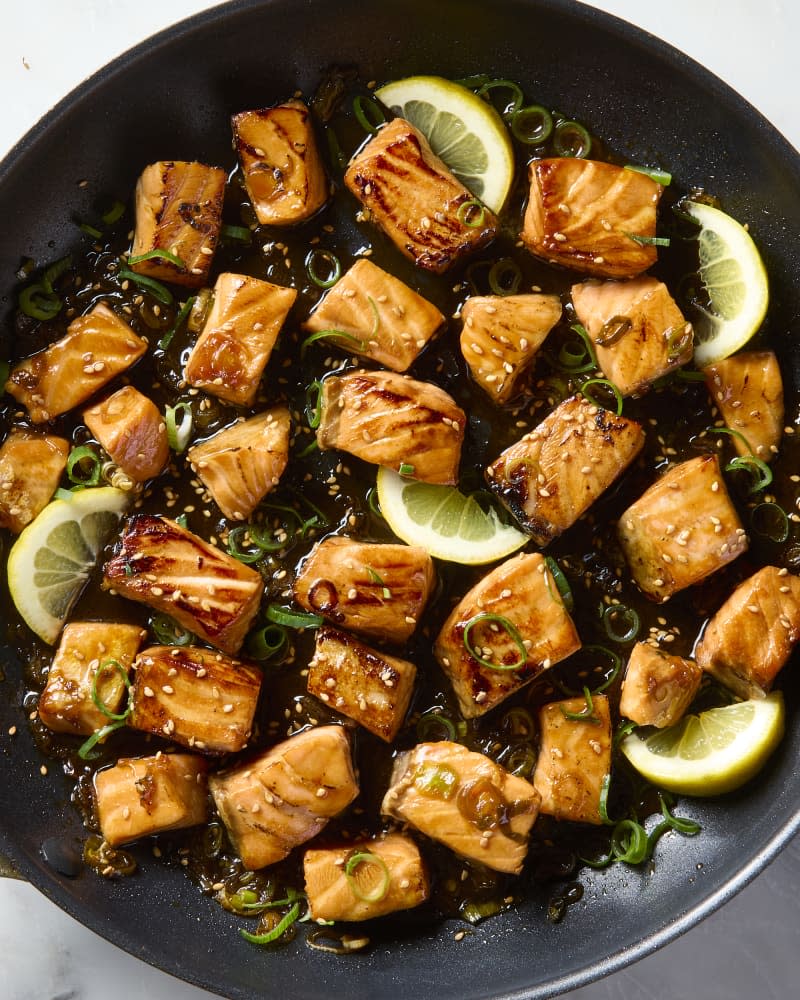 overhead shot of salmon bites in a pan, topped with sesame seeds, green onion and lemon wedges