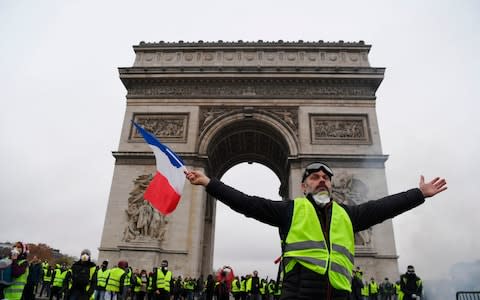 A demonstrator waves a French national flag during a protest of Yellow vests (Gilets jaunes) against rising oil prices and living costs in front of the Arc of Triomphe - Credit: AFP