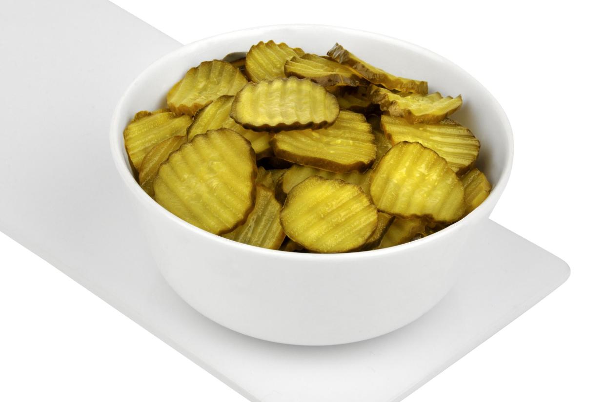 Sliced pickled cucumbers in bowl from above on white background.