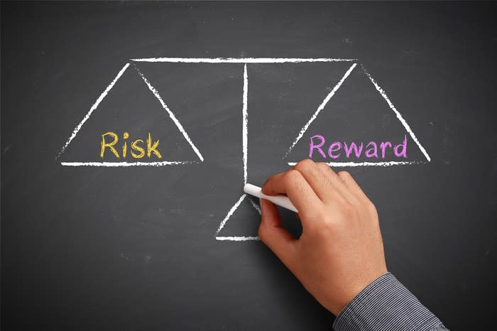 Man drawing scales with risk and reward on chalkboard.