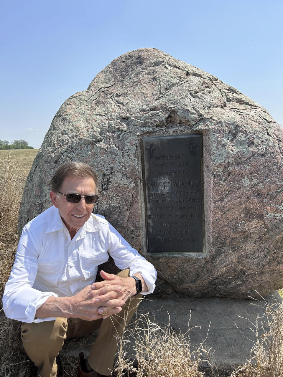 In this photo provided by Tom Heinz, the South Dakota businessman poses for a photo in front of a monument marking the first Catholic church in Brown County, South Dakota, on Friday, May 26, 2023. The church was founded by influential Catholic priest, the Rev. Robert W. Haire, who Heinz called the "father of the ballot initiative process" in his testimony earlier this year opposing a bill that would have created more restrictions for citizen-initiated constitutional amendments. (Courtesy Tom Heinz via AP)