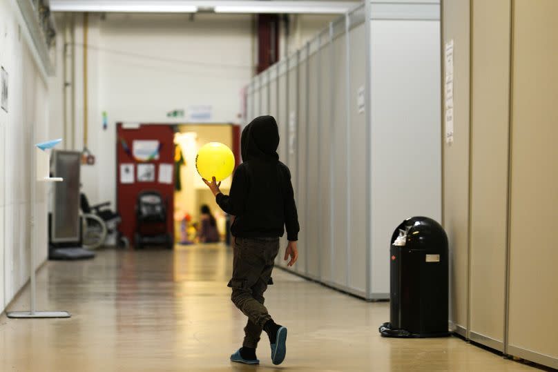 A boy with a ball walks alongside makeshift sleeping units inside the temporary refugee shelter at the former airport Tegel in Berlin, Germany, Nov. 9, 2022.