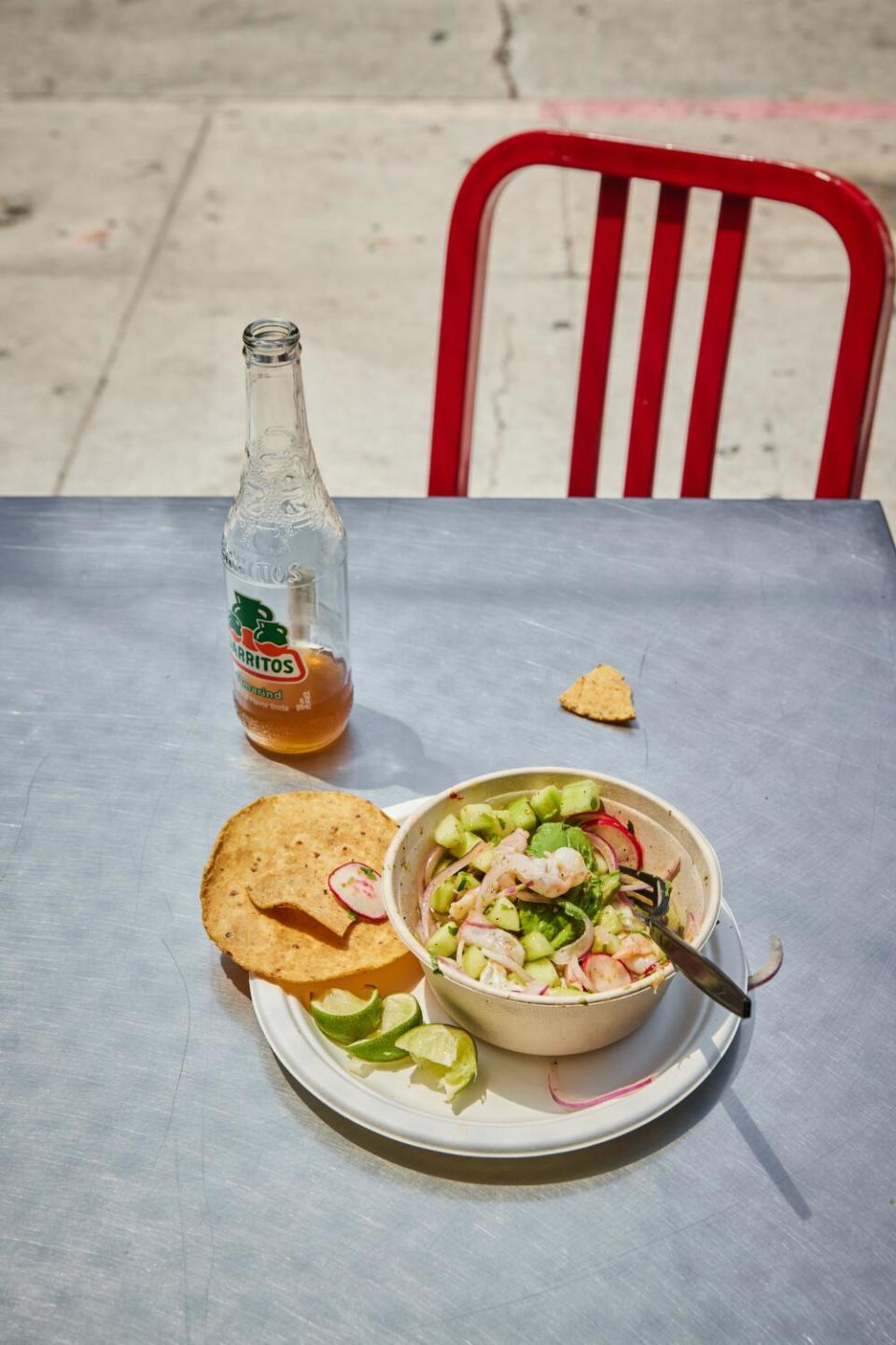 A plate of food sits next to a Jarritos bottle on a silver table outdoors.