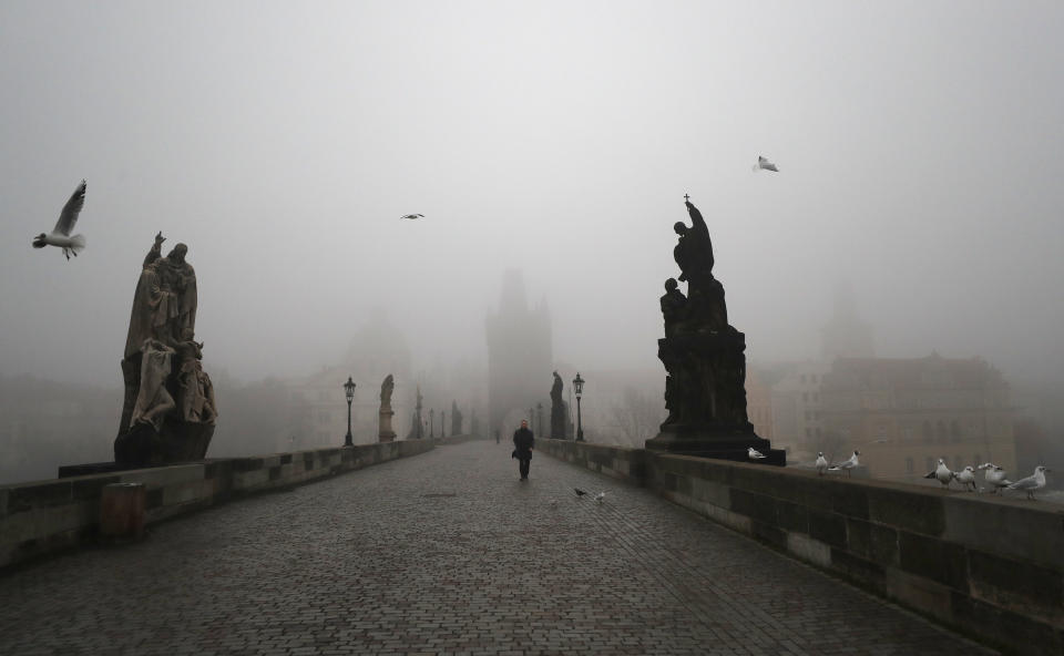 A man walks across the medieval Charles Bridge in Prague, Czech Republic, Wednesday, Feb. 24, 2021. The Czech government has decided to further tighten restrictive measures amid a surge of a highly contagious coronavirus variant in one of the hardest-hit European Union's nations. At the same time, the worsening situation has forced the Cabinet to abandon for now its plans to reopen all stores. (AP Photo/Petr David Josek)