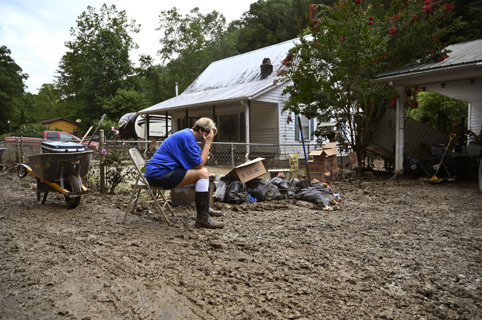 FILE - Teresa Reynolds sits exhausted as members of her community clean the debris from their flood ravaged homes at Ogden Hollar in Hindman, Ky., Saturday, July 30, 2022. Nearly a year after deadly widespread flooding hit eastern Kentucky, a housing crisis is affecting the impoverished region. Hundreds of Appalachian families remain displaced despite millions of federal dollars pouring in. (AP Photo/Timothy D. Easley)