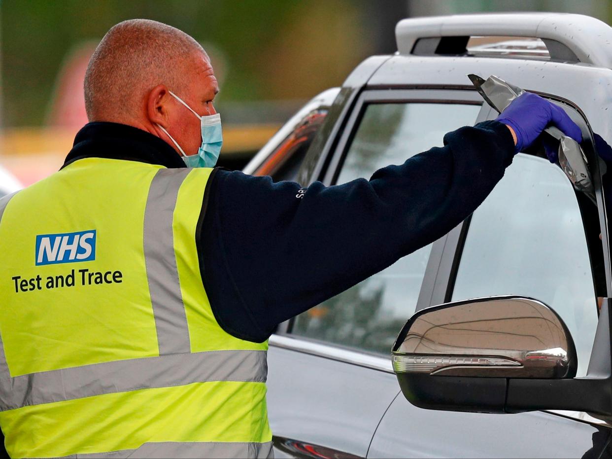 A driver receives a Covid-19 self-test kit from a worker wearing an NHS Test and Trace branded Hi-Vis jacket at a drive-in testing facility in Chessington (AFP via Getty Images)