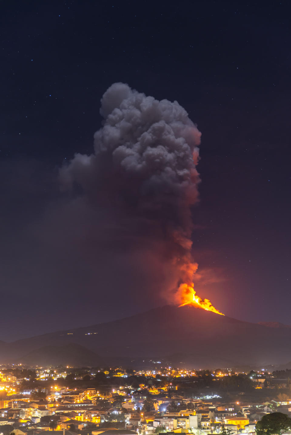 Flames and smoke billowing from a crater, as seen from the southern side of the Mt Etna volcano, tower over the city of Pedara, Sicily, Wednesday night, Feb. 24, 2021. Europe's most active volcano has been steadily erupting since last week, belching smoke, ash, and fountains of red-hot lava. (AP Photo/Salvatore Allegra)