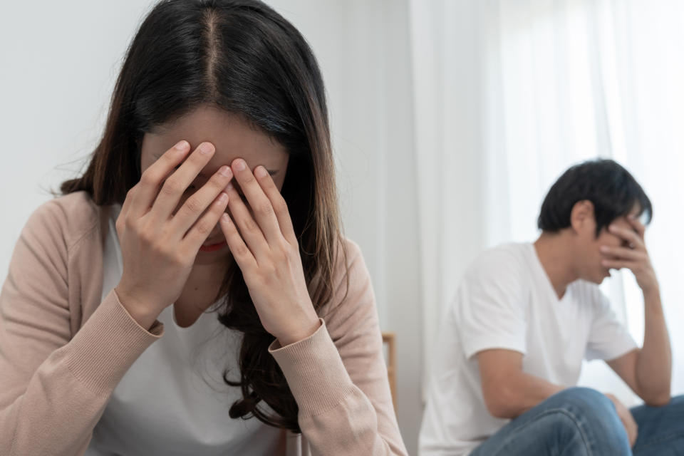 Two people indoors, with one in the foreground covering their face in distress and the other in the background also covering their face, showing a tense atmosphere