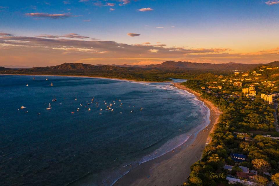 Aerial view of Tamarindo Beach in the orange sun glow. Can see boats and hillside buildings on this coast line of Costa Rica