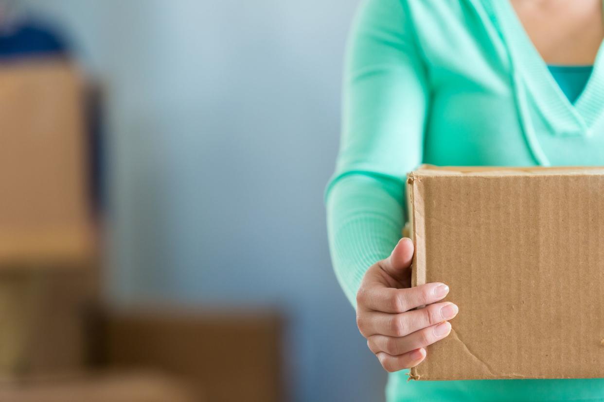 Woman holds box as she prepares to move or unpack. She is wearing a light green blouse. Woman is seen from the neck down. Copy space is available in the photo.