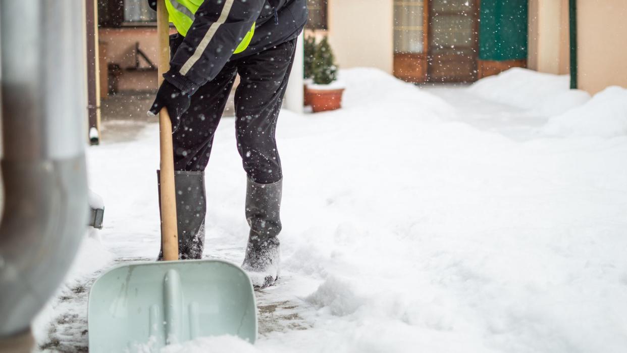 man with snow shovel cleans sidewalk