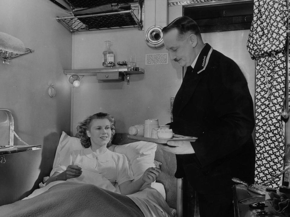 An LMS sleeping car attendant brings a passenger a morning cup of tea in 1945.