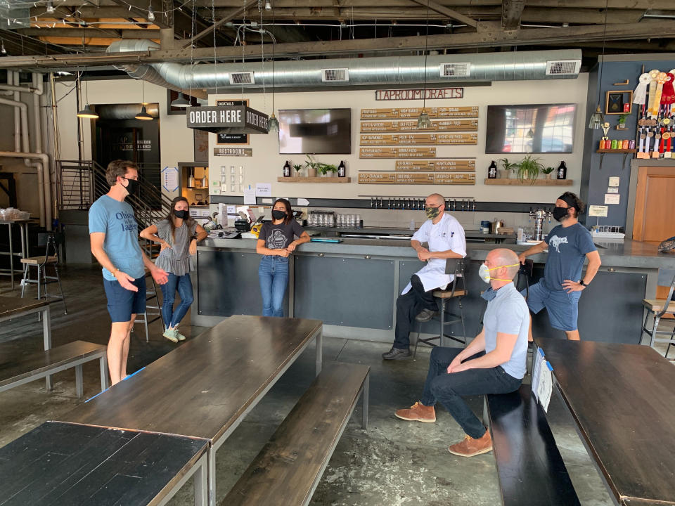 In a July 2020 photo provided by Wolf's Ridge Brewing, owner Bob Szuter, employees Allison Randolph and Alicia Herrmann, sous chef Andy Zamagias, general manager Corey Schlosser and employee Andy Powell, from left, gather inside the restaurant's tap room in Columbus, Ohio. Szuter says he’s trying to figure out new ways to bring in revenue, focusing more on the brewery side of the business until it’s safe to have a full dining room. (Charlie Wilkerson/Wolf's Ridge Brewing via AP)