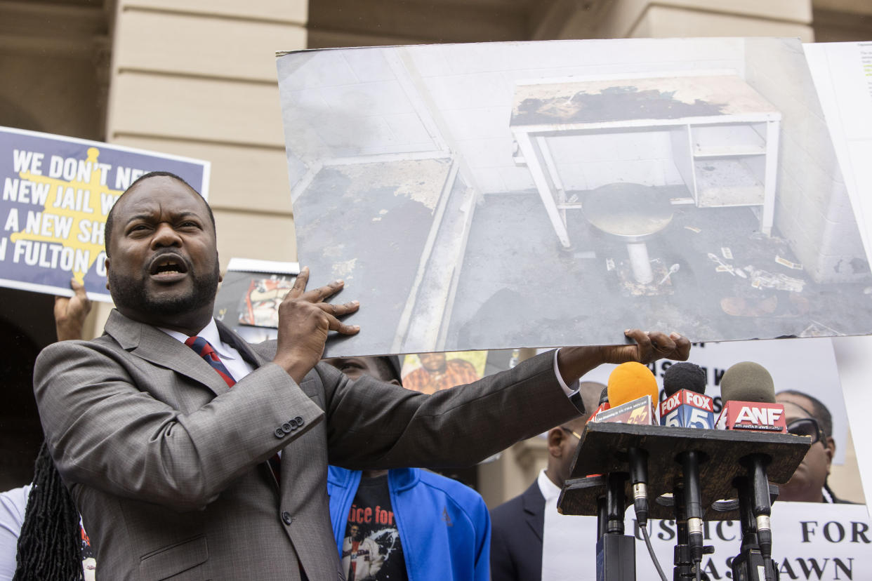 Attorney Michael Harper at the microphone, holding a poster showing the filthy conditions of the cell in which Lashawn Thompson died..