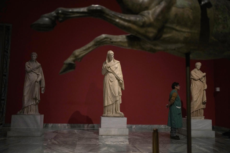 A cleaning woman stands between statues as she watches the presentation event for the planned renovation of the National Archaeological Museum in Athens, Greece, on Wednesday, Feb. 15, 2023. The British architect, David Chipperfield, is leading the project that will expand the museum's exhibition space, create a new entrance, and garden space. The museum, which showcases artifacts from ancient Greece, is considered to be one of the most important in the world. (AP Photo/Thanassis Stavrakis)