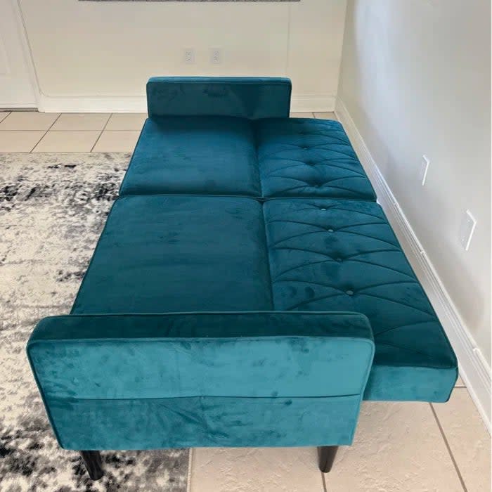 Reviewer's photo of the velvet tufted sofa in the color teal with its back folded down to create a sofa bed