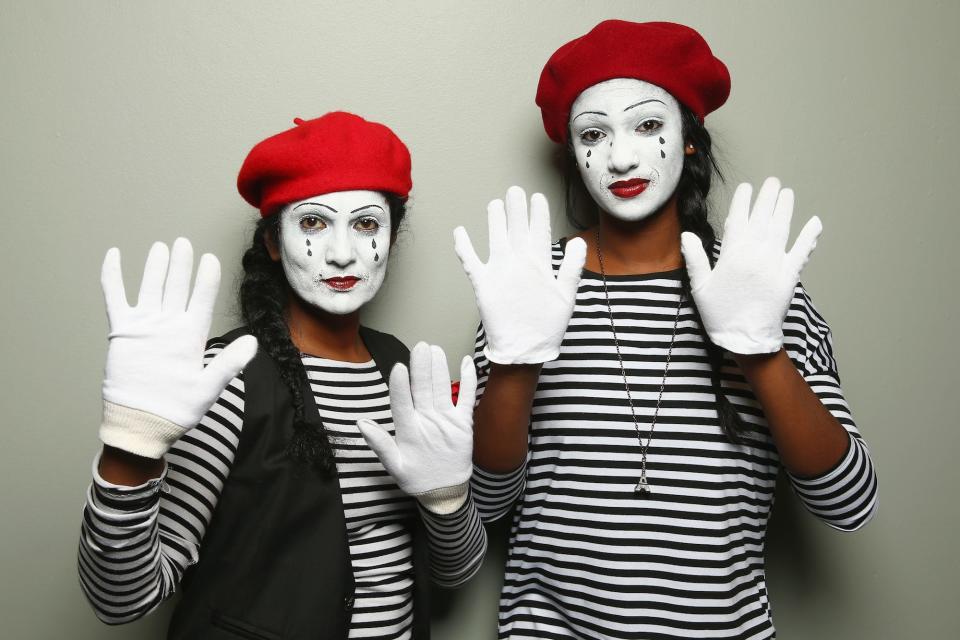 Two people dressed as mimes in striped black and white shirts, white face paint, and red hats