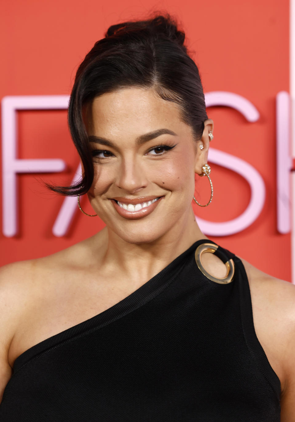 Ashley Graham was all smiles at the red carpet event in a black one-shoulder dress with gold ring detailing on the straps.