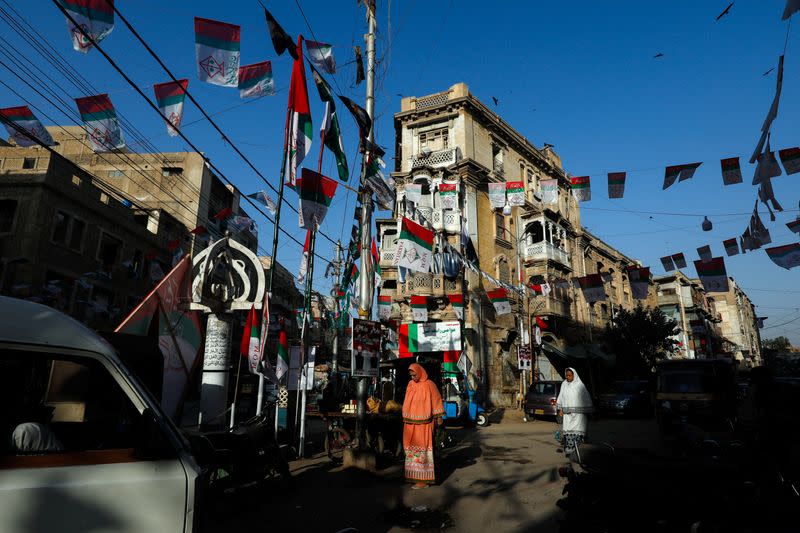 Women walk along a street, decorated with campaign flags of political parties, ahead of general elections, in Karachi