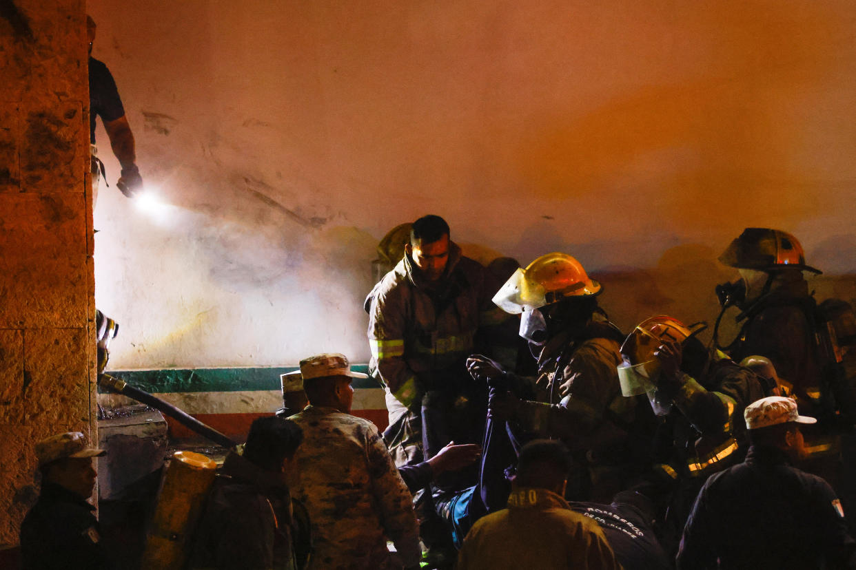 Service members and firefighters gather at what appears to be an indoor smoke-filled stairway.