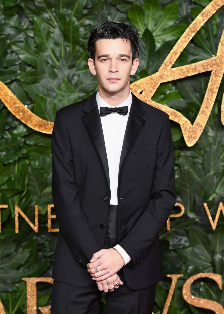 Matty in classic tuxedo and bow tie standing at event with leafy backdrop