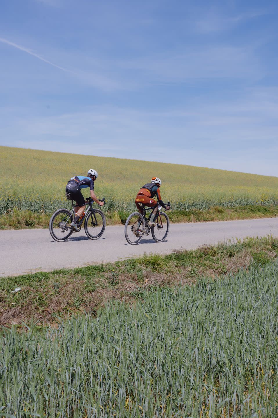 two cyclists, one on team amani, ride along a farm road in spain