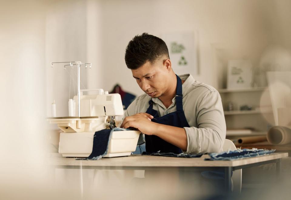 focused tailor sewing on a machine young fashion designer stitching a piece of denim mixed race tailor using a sewing machine creative businessman working in his design workshop