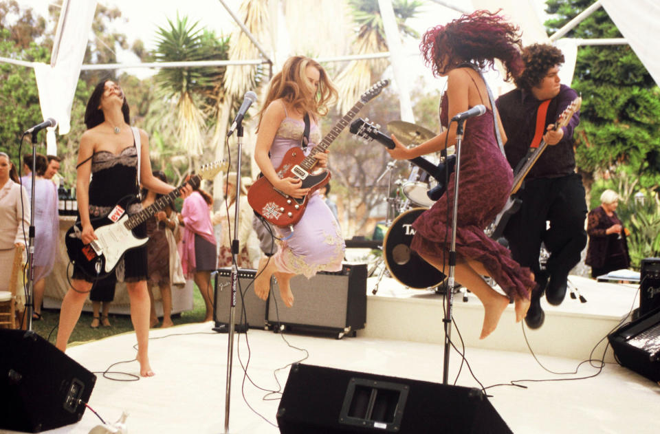 Liv Tyler, Jennifer Connelly, Coyote Shivers and Gina Gershon perform energetically in a band, all jumping around in the air on stage with instruments