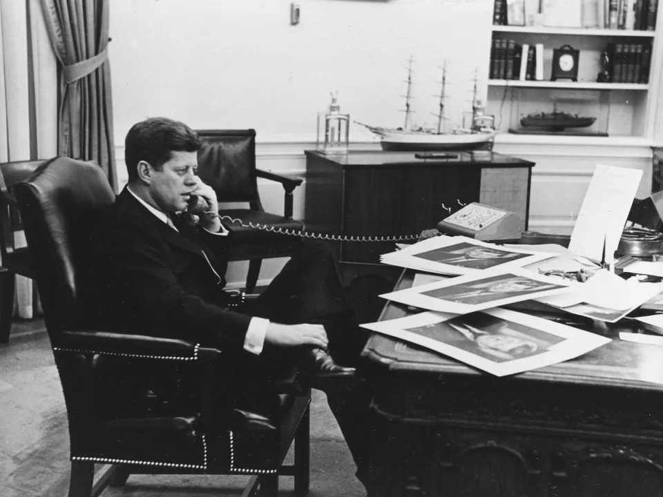 President John F. Kennedy in the Oval Office signing copies of his official portrait in 1961.