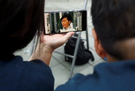 People use mobile phone to watch a news conference, as they gather to wait for a government announcement regarding the proposed extradition bill, near the Legislative Council building in Hong Kong