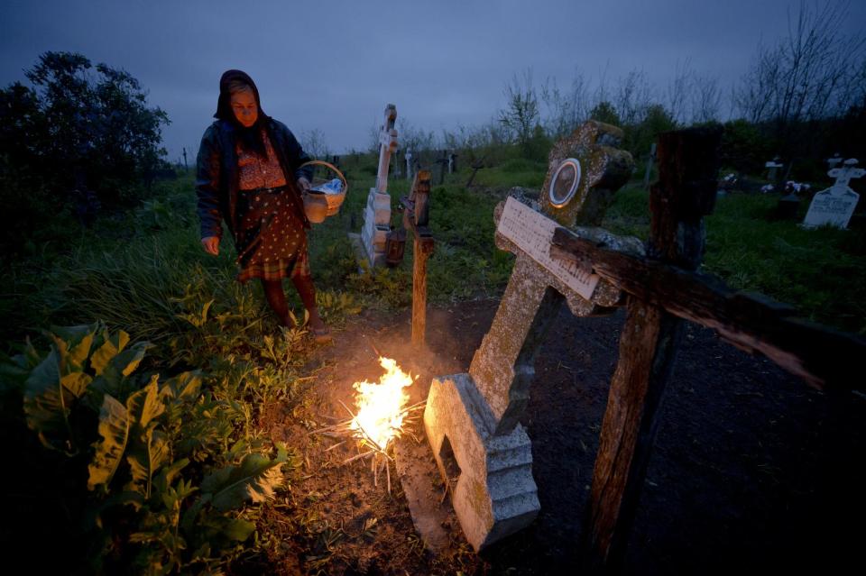 A woman stands by a fire she lit near a grave in the village of Copaciu, southern Romania, early Thursday, April 17, 2014. Part of a Holy Week tradition, Romanians visit, on Maundy Thursday, the graves of their loved ones, light fires and share food with community members in memory of the departed. Orthodox and Catholic worshipers celebrate Easter on on April 20.(AP Photo/Andreea Alexandru/ Mediafax) ROMANIA OUT