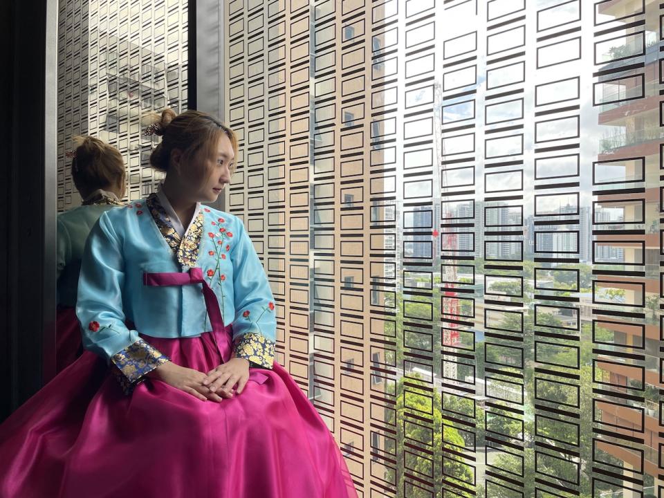 Lady in a blue and pink hanbok (traditional ethnic Korean clothing) looking out of a window