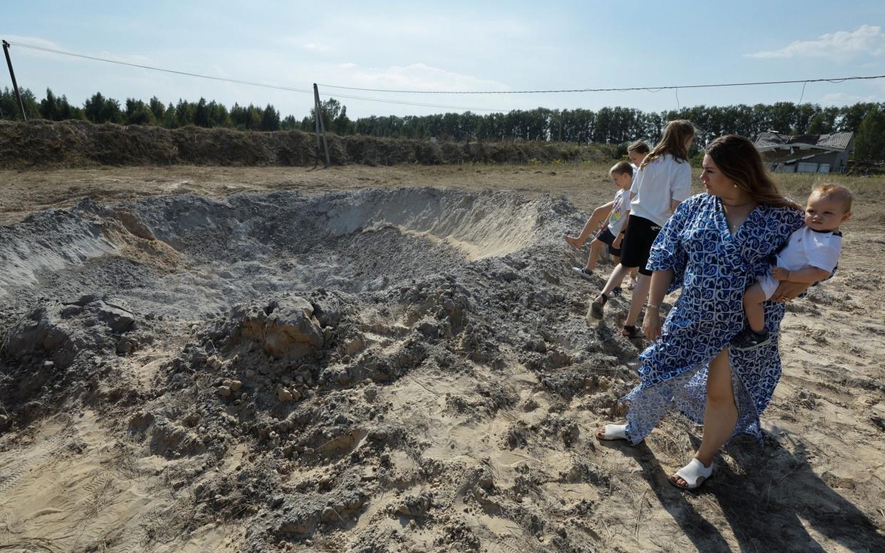 Locals view a bomb crater following a Russian missile strike in a village outside of Kyiv