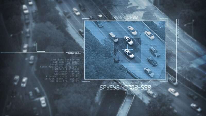 An overhead surveillance shot of a car in traffic, as captured by a drone, helicopter, or satellite.