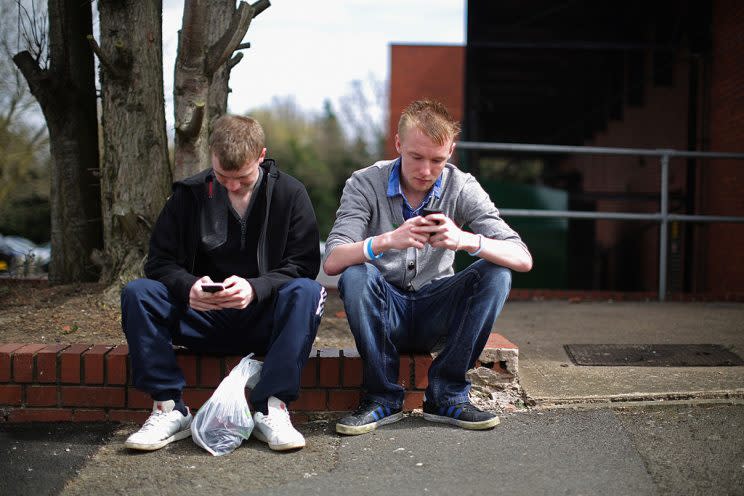 CORBY, ENGLAND - APRIL 24: Two youths send text messages on their smart phones in Corby, Northamptonshire, the youth unemployment capital of Britain, on April 24, 2013 in Corby, England. (Photo by Christopher Furlong/Getty Images)