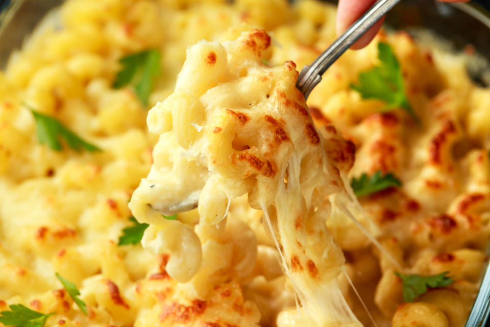 A spoon lifts sticky macaroni and cheese, garnished with parsley, from a casserole dish