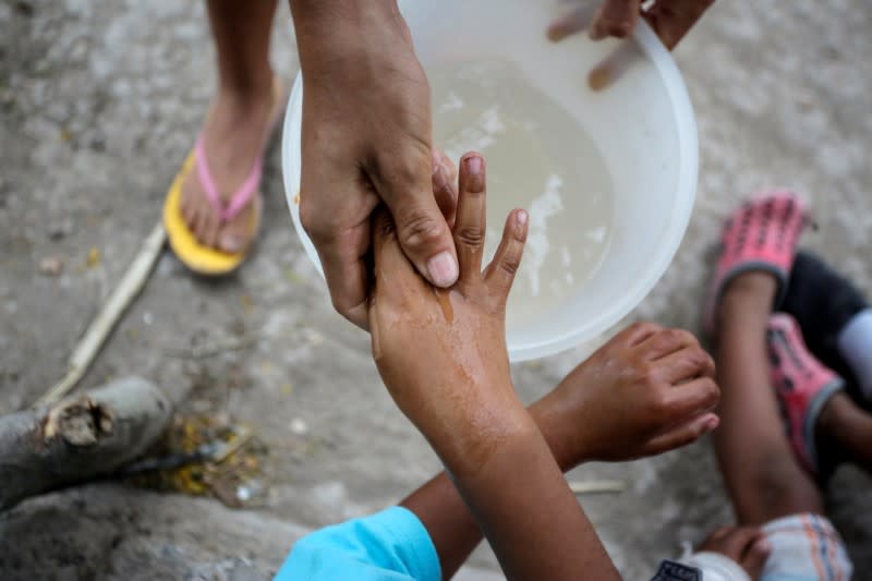 A Central American migrant washes the hands of a child at an encampment of more than 2,000 migrants seeking asylum in the U.S., as local authorities prepare to respond to the coronavirus disease (COVID-19) outbreak, in Matamoros
