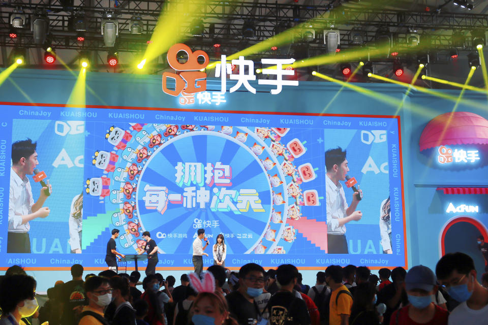 In this July 31, 2020, photo, people watch a performance presented by Chinese technology firm Kuaishou at the ChinaJoy expo in Shanghai. China's internet watchdog has fined technology platforms operated by e-commerce company Alibaba and gaming firm Tencent for spreading sexually suggestive content involving children, as regulators sought to clean up the internet of content harmful to minors. (Chinatopix via AP)