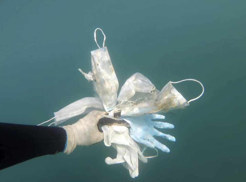 Fotografía tomada el 21 de mayo de 2020 y proporcionada el miércoles 27 de mayo de 2020 por el grupo ambientalista Operation Mer Propre (Operación mar limpio) de un buzo sosteniendo guantes y mascarillas encontrados en el lecho del Mediterráneo cerca del centro turístico en la rivera francesa de Antibes. (Operation Mer Propre vía AP)