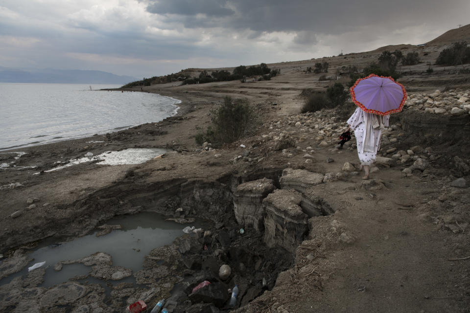 FILE - In this April 2, 2017 file photo, a woman walks next to sinkholes along the Dead Sea shore near the Israeli Kibbutz of Ein Gedi. The Dead Sea, which is actually a salty lake situated at the lowest place on earth, is slowly shrinking as a result of years of water diversion from the Jordan River and damage caused by mineral-extraction companies. Israel’s new environmental protection minister, Tamar Zandberg is actively involved in negotiations to ensure that Dead Sea factories, which are among Israel’s worst polluters, address environmental concerns as licenses are renewed in the coming years, (AP Photo/Oded Balilty, File)