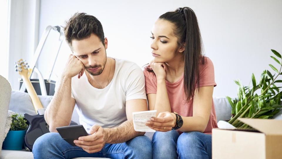 Serious couple sitting on couch in new home checking bills