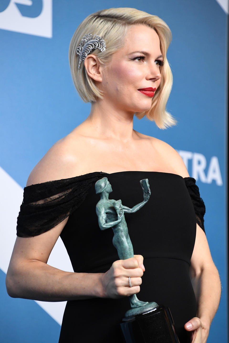 Michelle Williams poses in the press room wearing a black dress and rhinestone feather pin in her hair after winning the award for Outstanding Performance by a Female Actor in a Television Movie or Limited Series for 