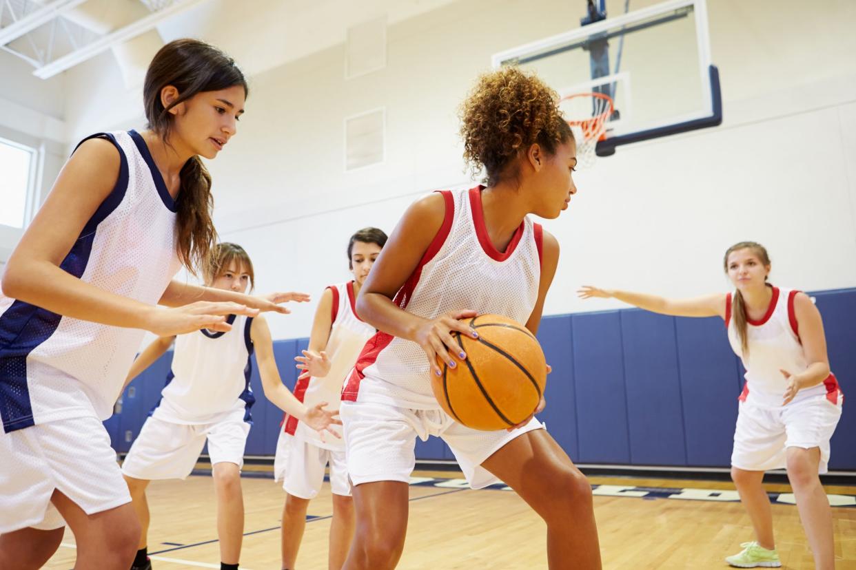 Female High School Basketball Team Playing Game In Gymnasium