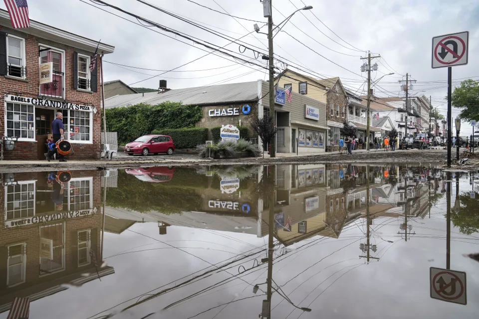 Residents, journalists, and emergency service workers walk around a flooded Main Street, Monday, July 10, 2023, in Highland Falls, N.Y. Heavy rain has washed out roads and forced evacuations in the Northeast as more downpours were forecast throughout the day. One person in New York's Hudson Valley has drowned as she was trying to leave her home. (AP Photo/John Minchillo)