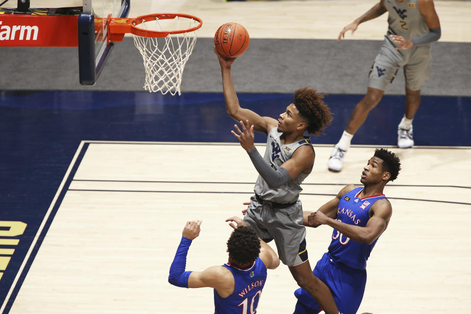 West Virginia guard Miles McBride (4) shoots while defended by Kansas forward Jalen Wilson (10) and guard Ochai Agbaji (30) during the first half of an NCAA college basketball game Saturday, Feb. 6, 2021, in Morgantown, W.Va. (AP Photo/Kathleen Batten)