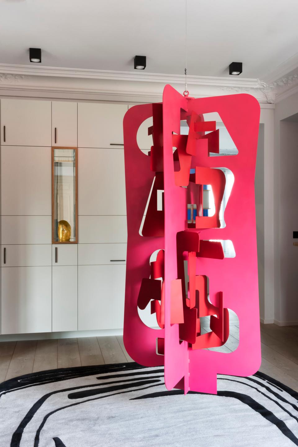 The entrance gallery is decorated with a pink-and-red lacquered aluminum sculpture called Wings of Desire, created by Frédéric Crouzet and suspended above a black-and-white carpet designed by Réda Amalou at Toulemonde Bochart.