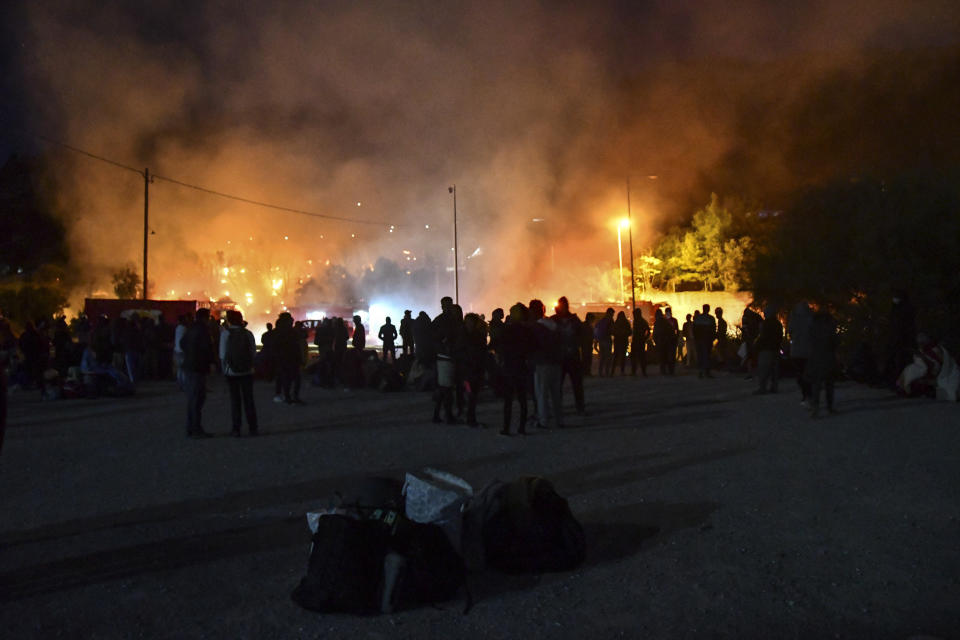 People look at a fire at a refugee and migrant camp, on the Greek island of Samos, Greece, Monday, Nov. 2, 2020. Dozens of accommodations were destroyed by the fire which broke out in the early hours on Monday, three days after an earthquake hit the island. (AP Photo/Michael Svarnias)